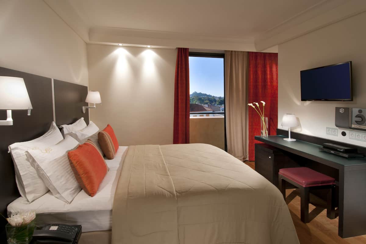 A hotel room with a bed, desk, TV, and a view of the outdoors.