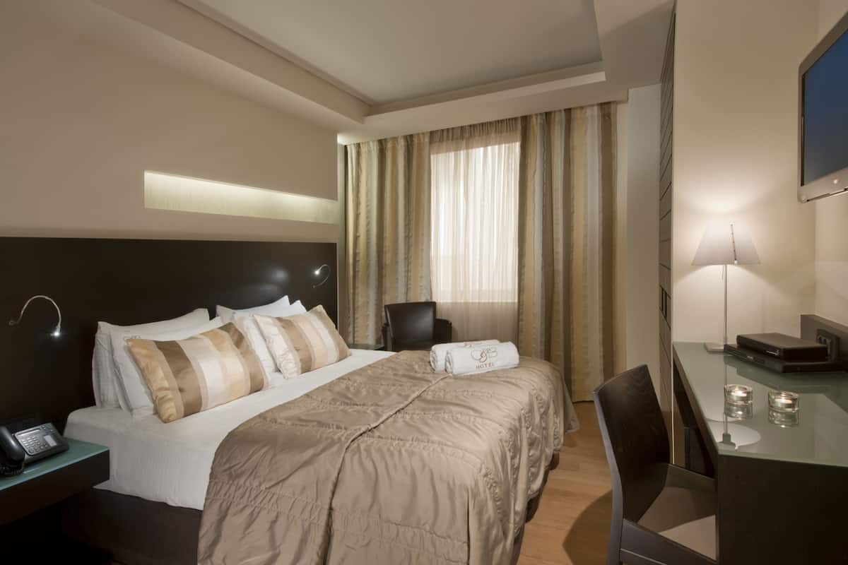 A hotel room with a bed, bedside table with a phone, a desk with a lamp, and a chair.