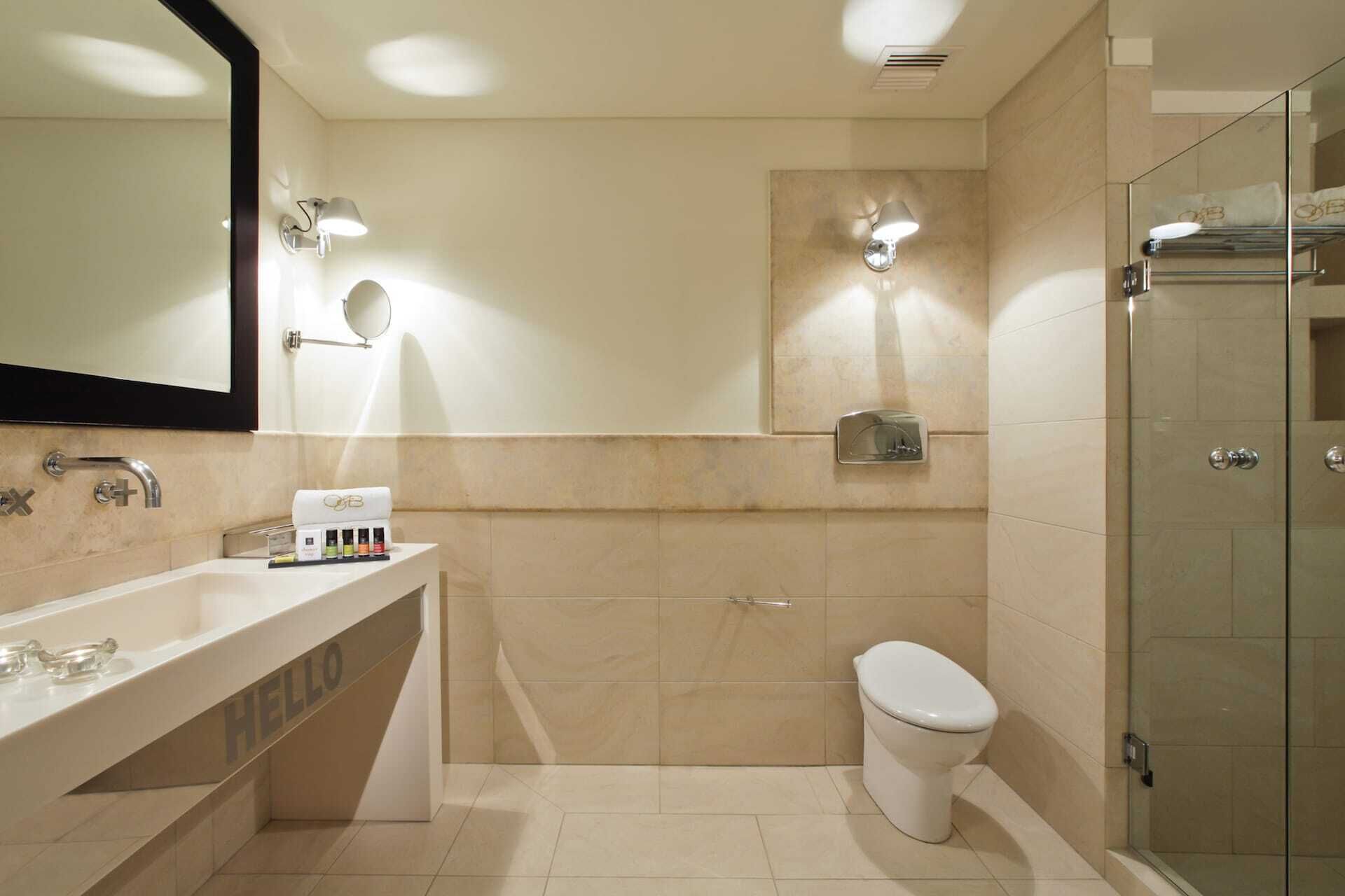 A modern bathroom with a large mirror, a vanity with toiletries, a toilet, and a glass-enclosed shower area.