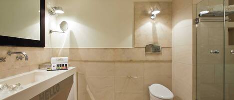 A modern bathroom with a large mirror, a vanity with toiletries, a toilet, and a glass-enclosed shower area.