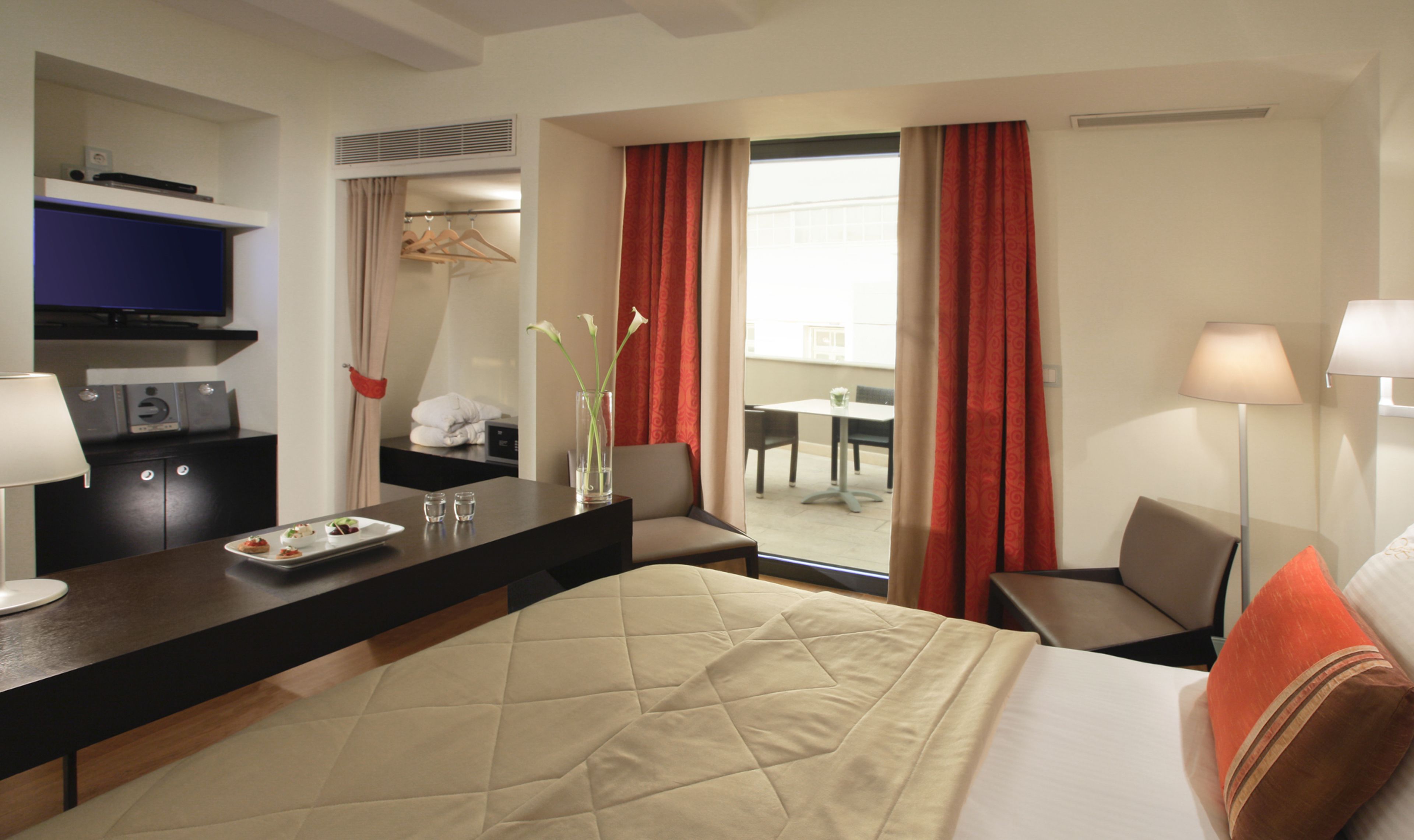 Ein Hotelzimmer mit Bett, Schreibtisch mit Computer, Stuhl, Tisch und einem Fenster mit Vorhängen.