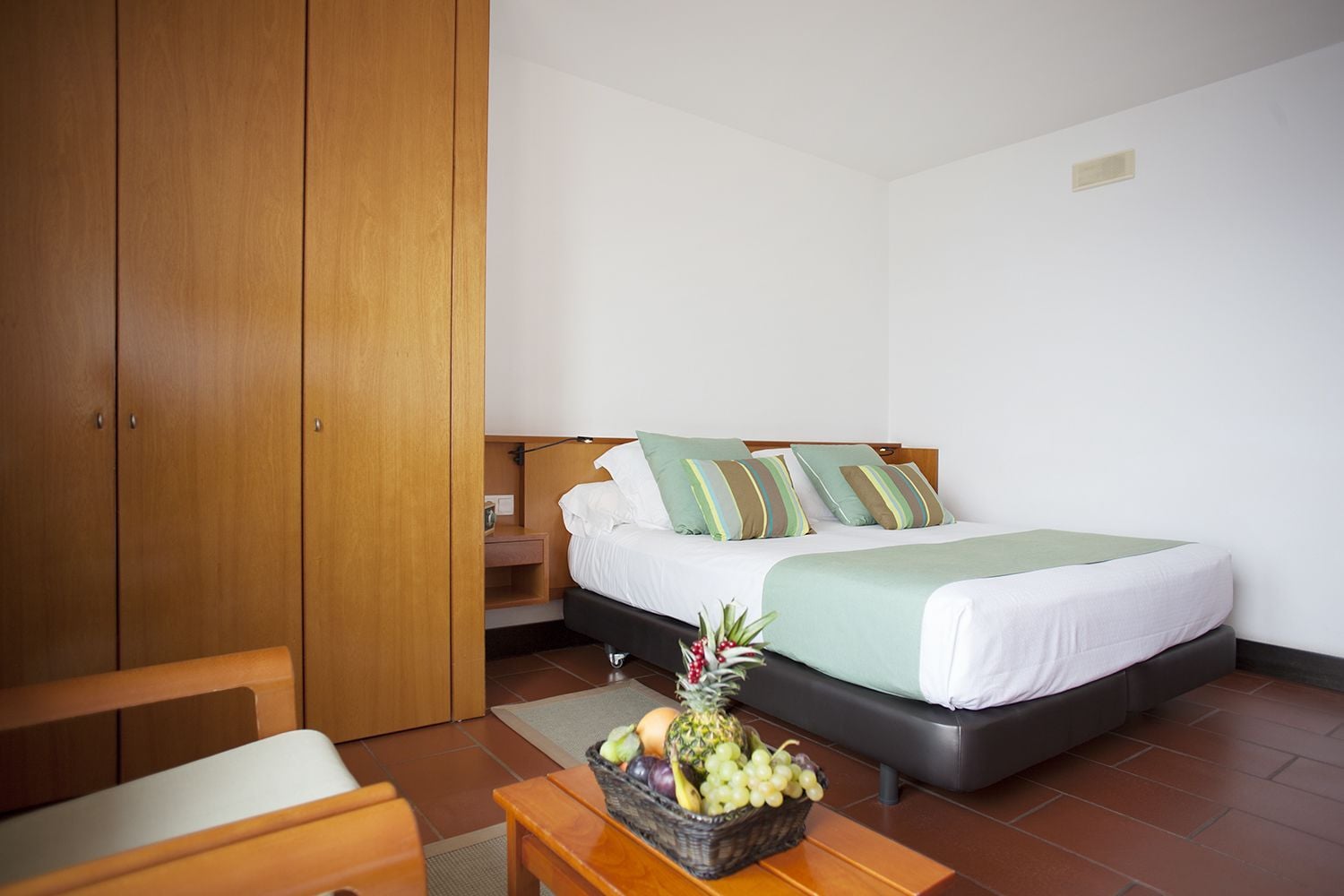 Un dormitorio con cama, armario de madera y una mesa con fruta.