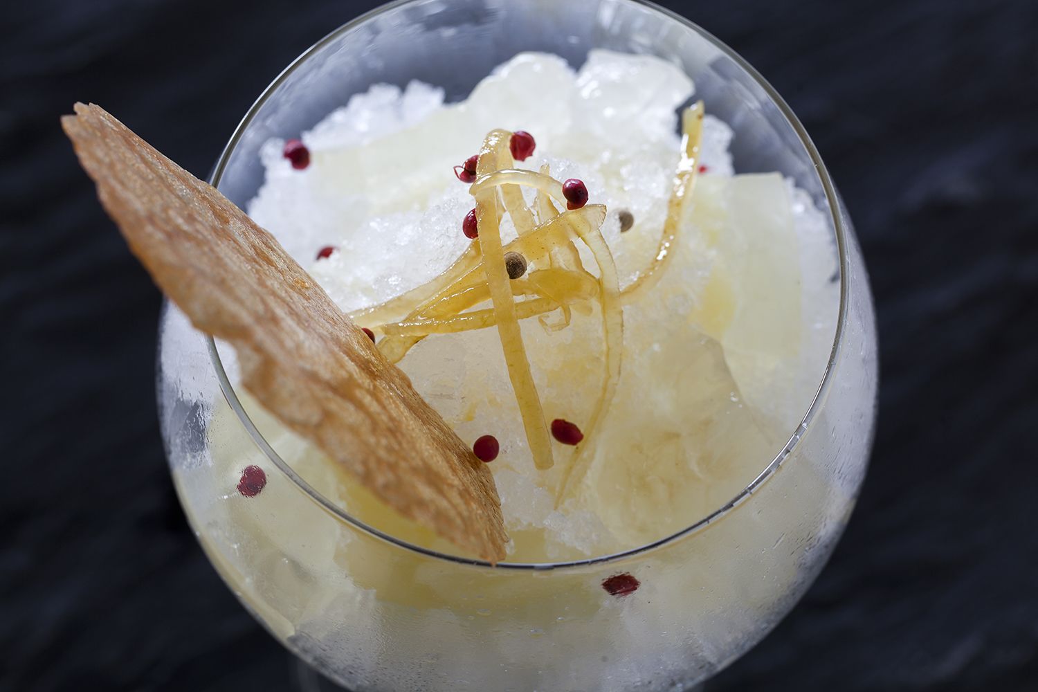 A cocktail with ice cubes, lemon slices, and a garnish on a dark background.