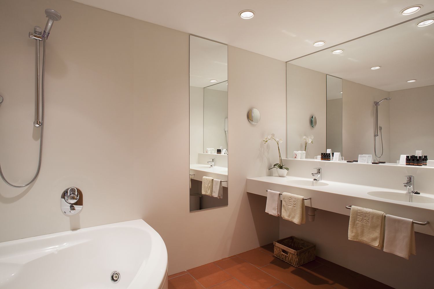 Een moderne badkamer met een badkuip, twee wastafels, een grote spiegel en een douche.