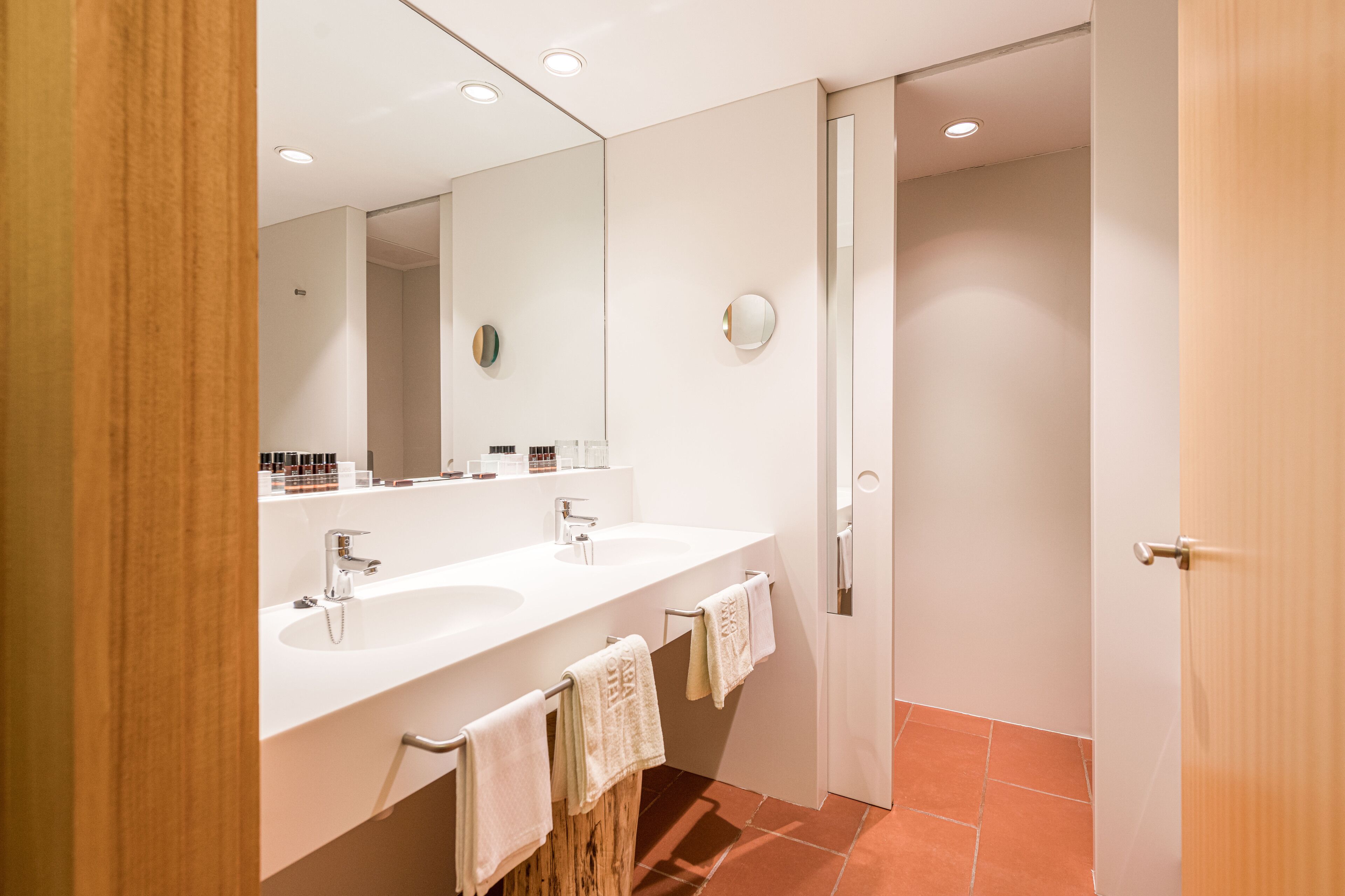 A modern bathroom with two sinks, a large mirror, and a door leading to another room.