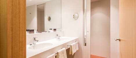 A modern bathroom with two sinks, a large mirror, and a door leading to another room.