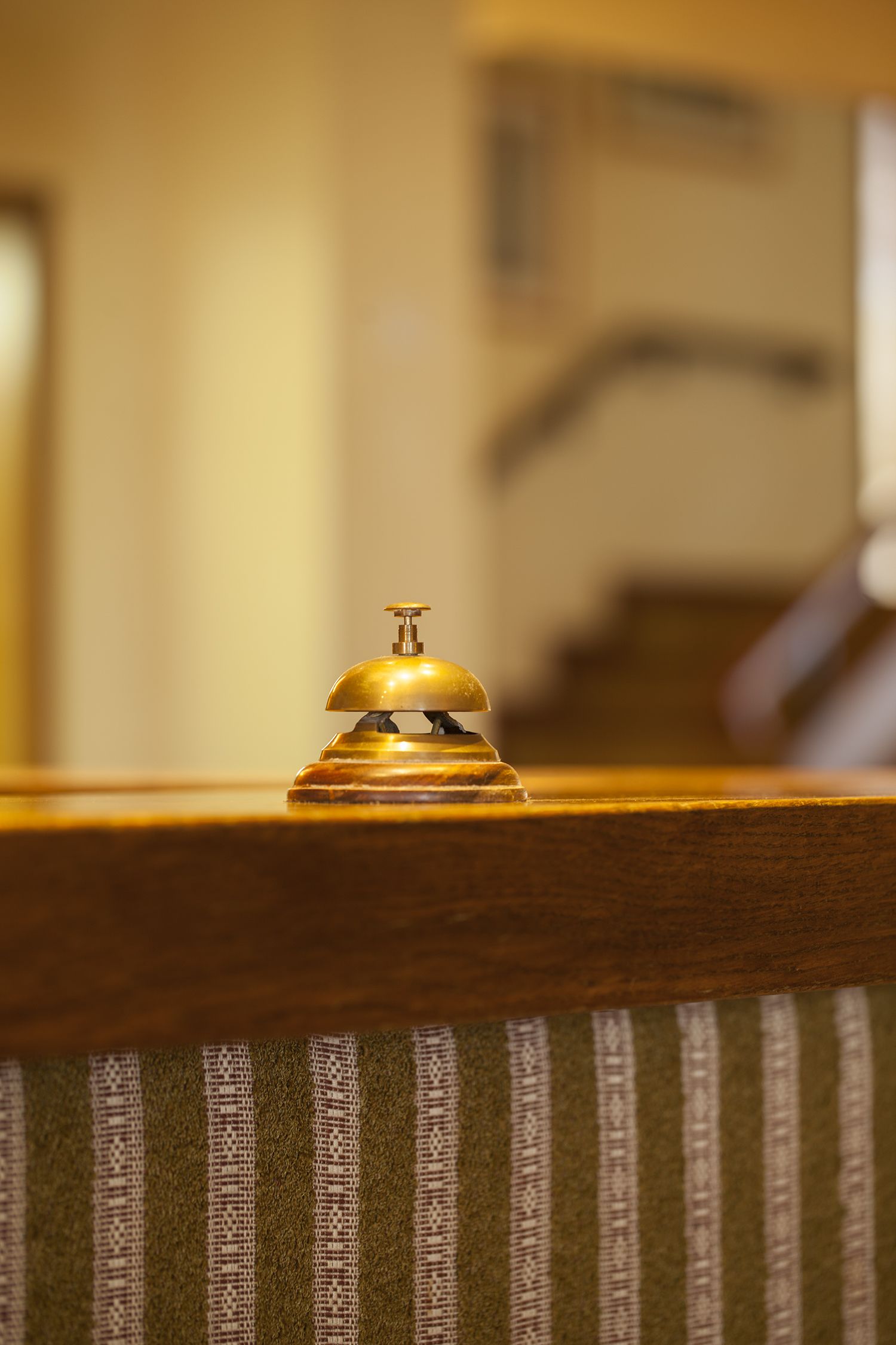 Un gros plan d’une cloche en laiton fixée à une rambarde en bois, avec un arrière-plan flou qui suggère un décor intérieur.
