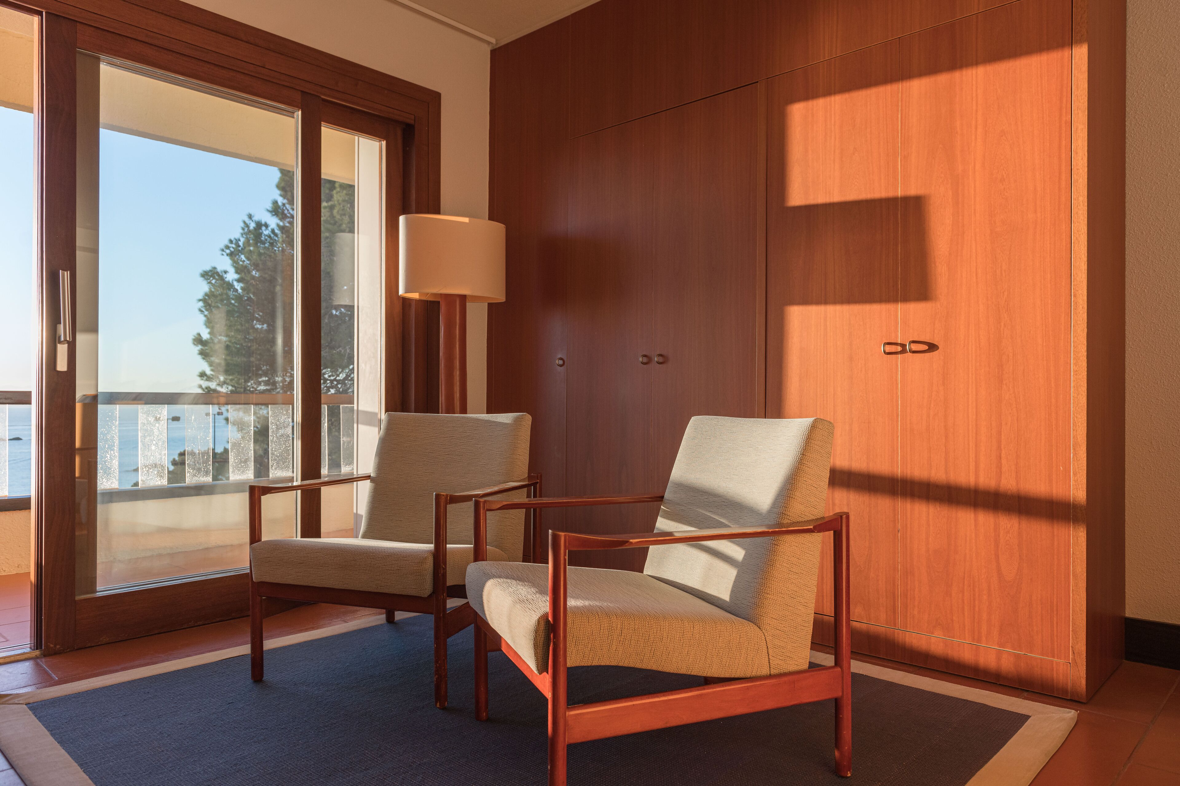 A room with two wooden chairs, a floor lamp, and a large wooden wardrobe.