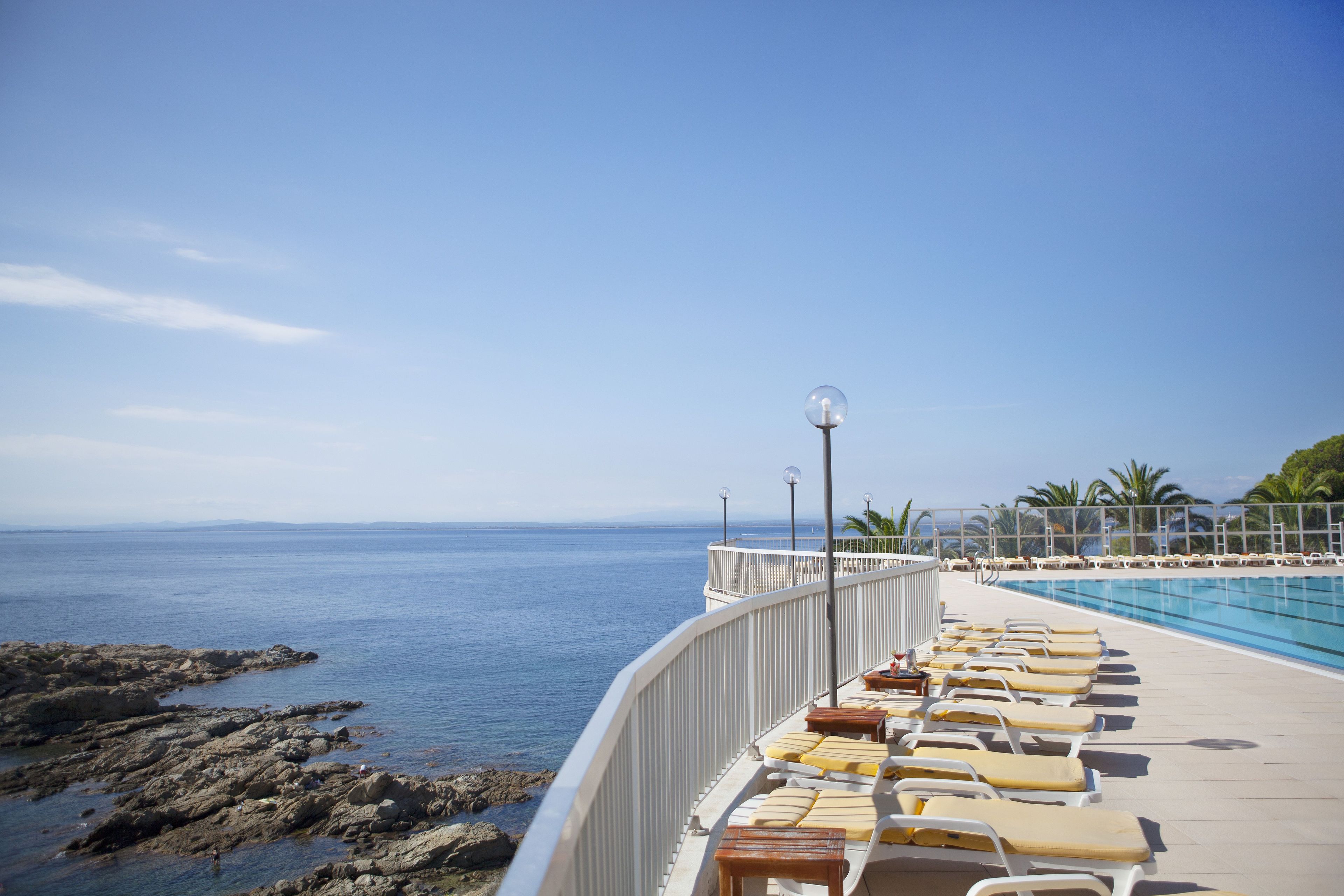 Zona junto a la piscina con sillones de descanso y vista al mar.