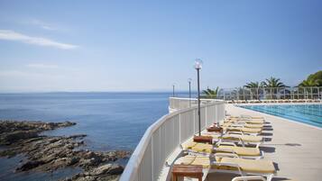 Zona junto a la piscina con sillones de descanso y vista al mar.