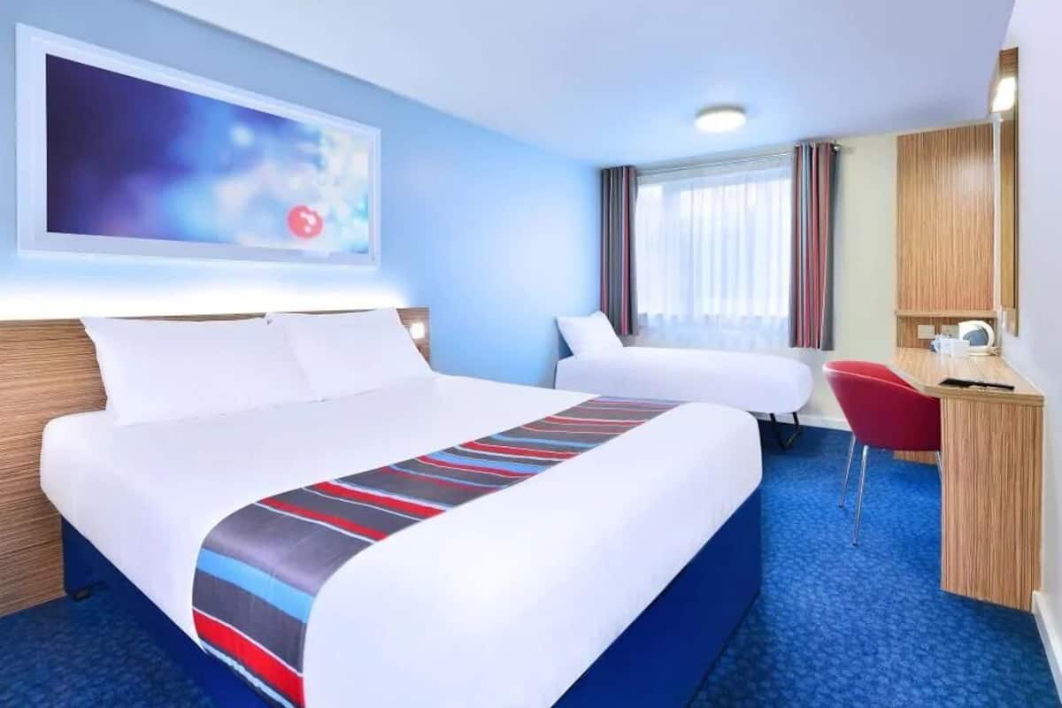 A hotel room with a large bed, a smaller bed, a desk, and a TV mounted on the wall.