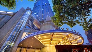 A modern hotel entrance with a curved glass facade and a prominent building in the background. - Sofitel Nanjing Galaxy Suning (Nanjing)