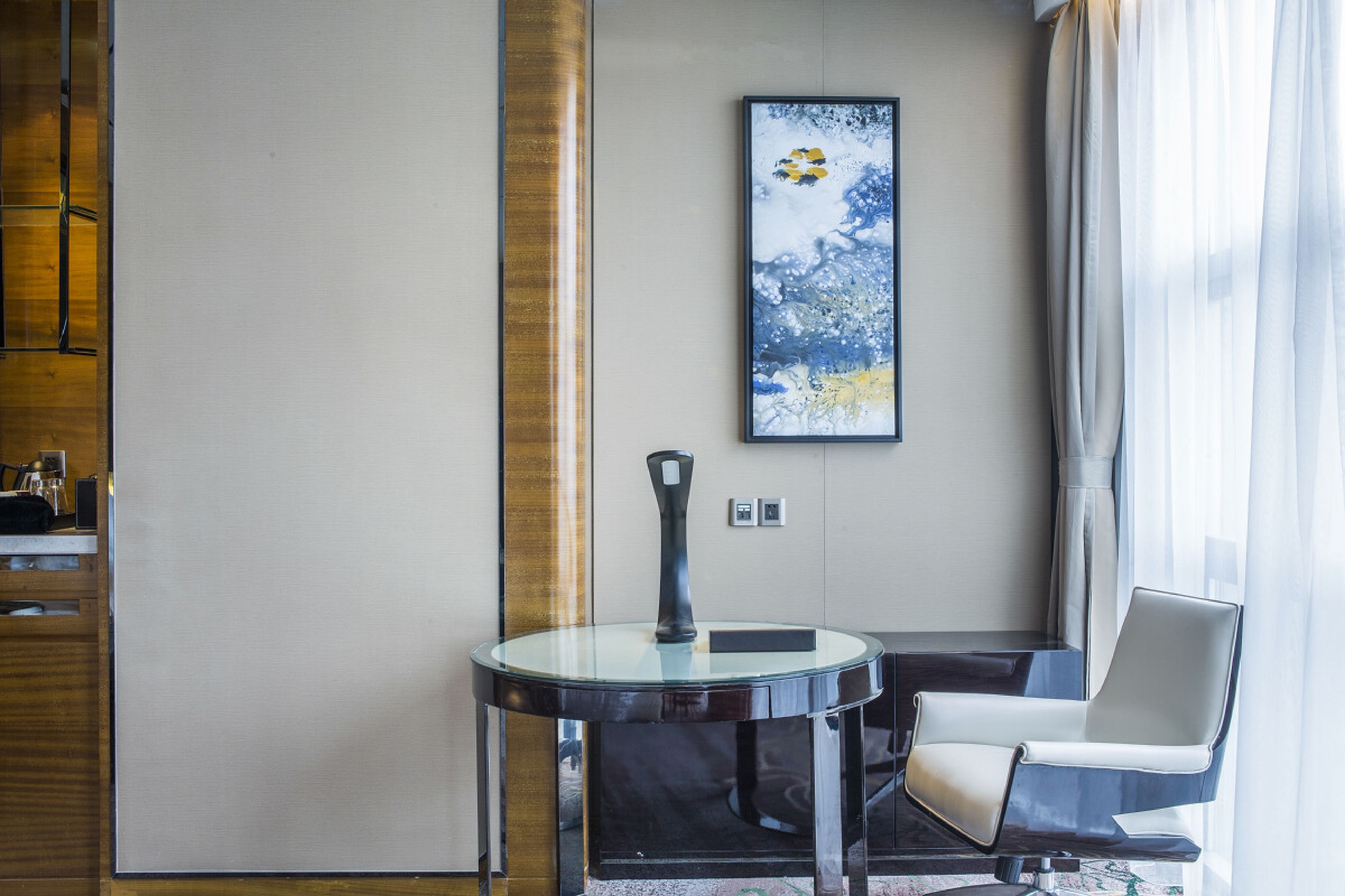 Een moderne hotelkamer met een ronde glazen tafel, een witte stoel, een groot abstract schilderij aan de muur en een houten accentmuur.