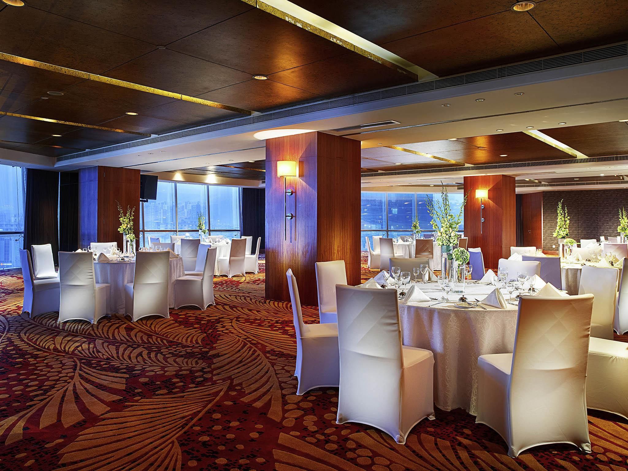 Un amplio salón de banquetes con mesas redondas, sillas blancas y una alfombra estampada.