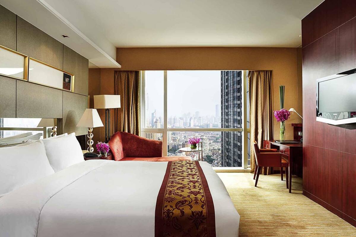Habitación de hotel con una cama grande, un escritorio, una silla, un televisor y vistas a la ciudad.