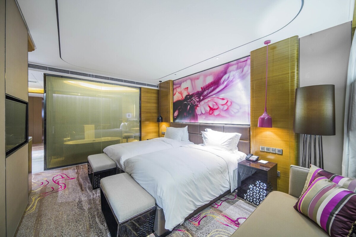 Una habitación de hotel moderna con una cama grande, una mesita de noche, un sofá y un ventanal amplio.