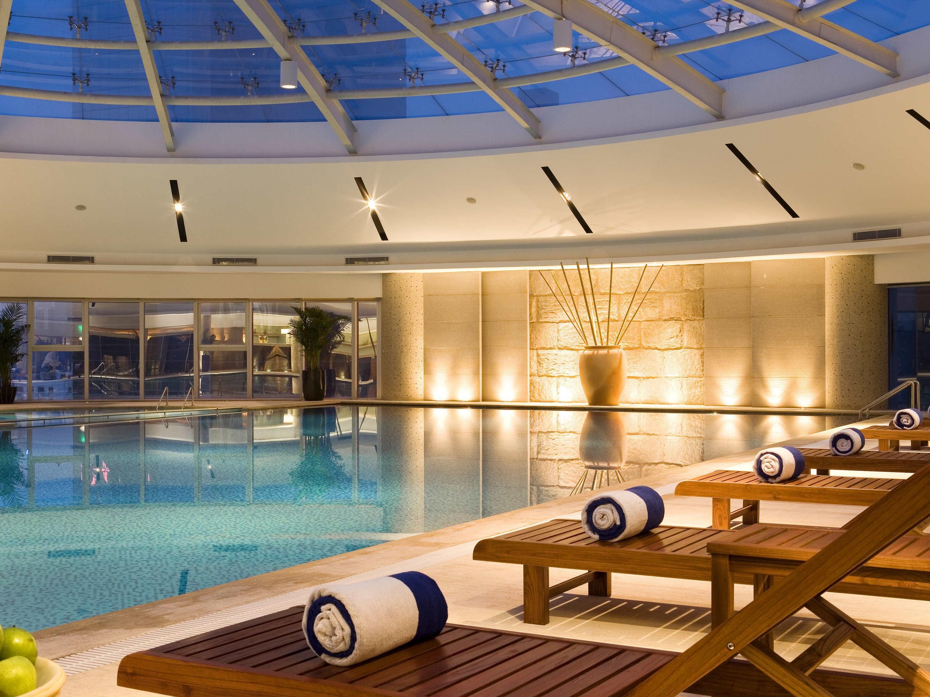 An indoor swimming pool with lounge chairs and a glass ceiling.