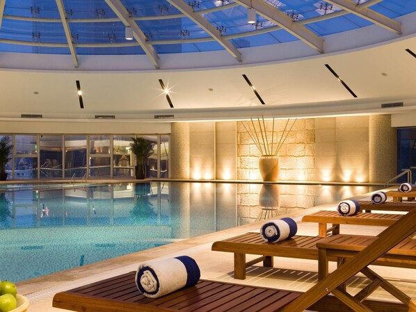 Piscina interior con sillones de descanso y techo de vidrio.