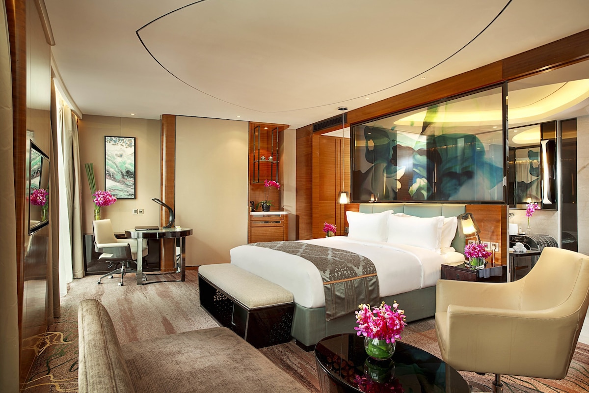 Una habitación de hotel moderna con una cama grande, un escritorio, una silla y una mesita con un jarrón de flores.