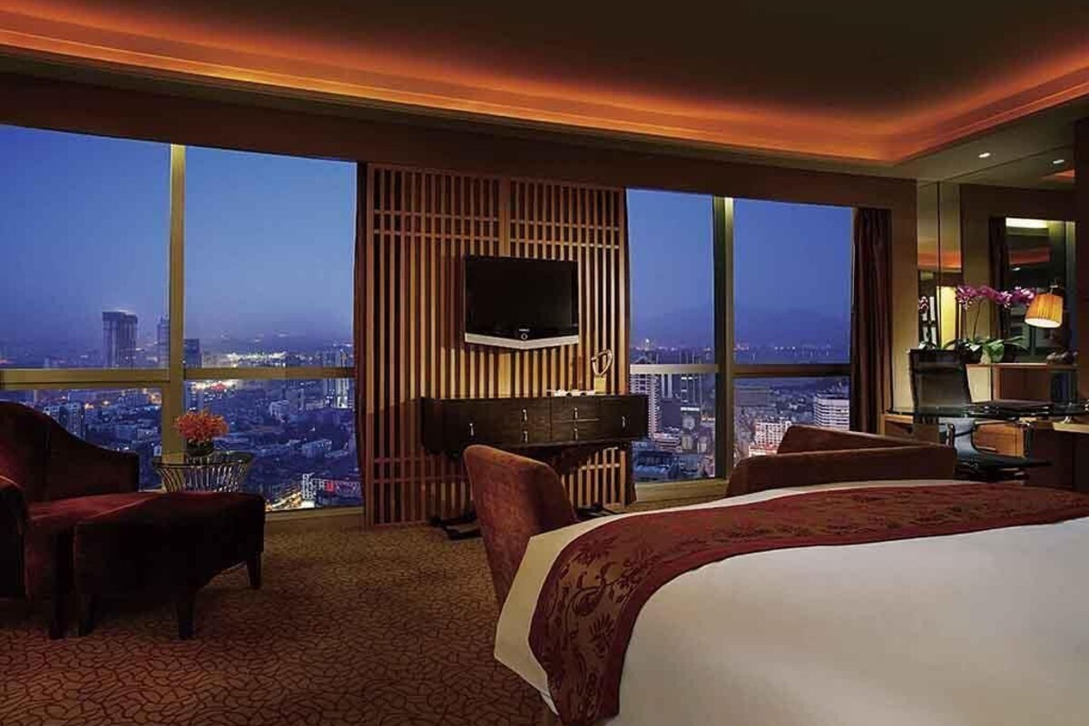 Habitación de hotel con una cama grande, televisión, escritorio y vista a la ciudad.
