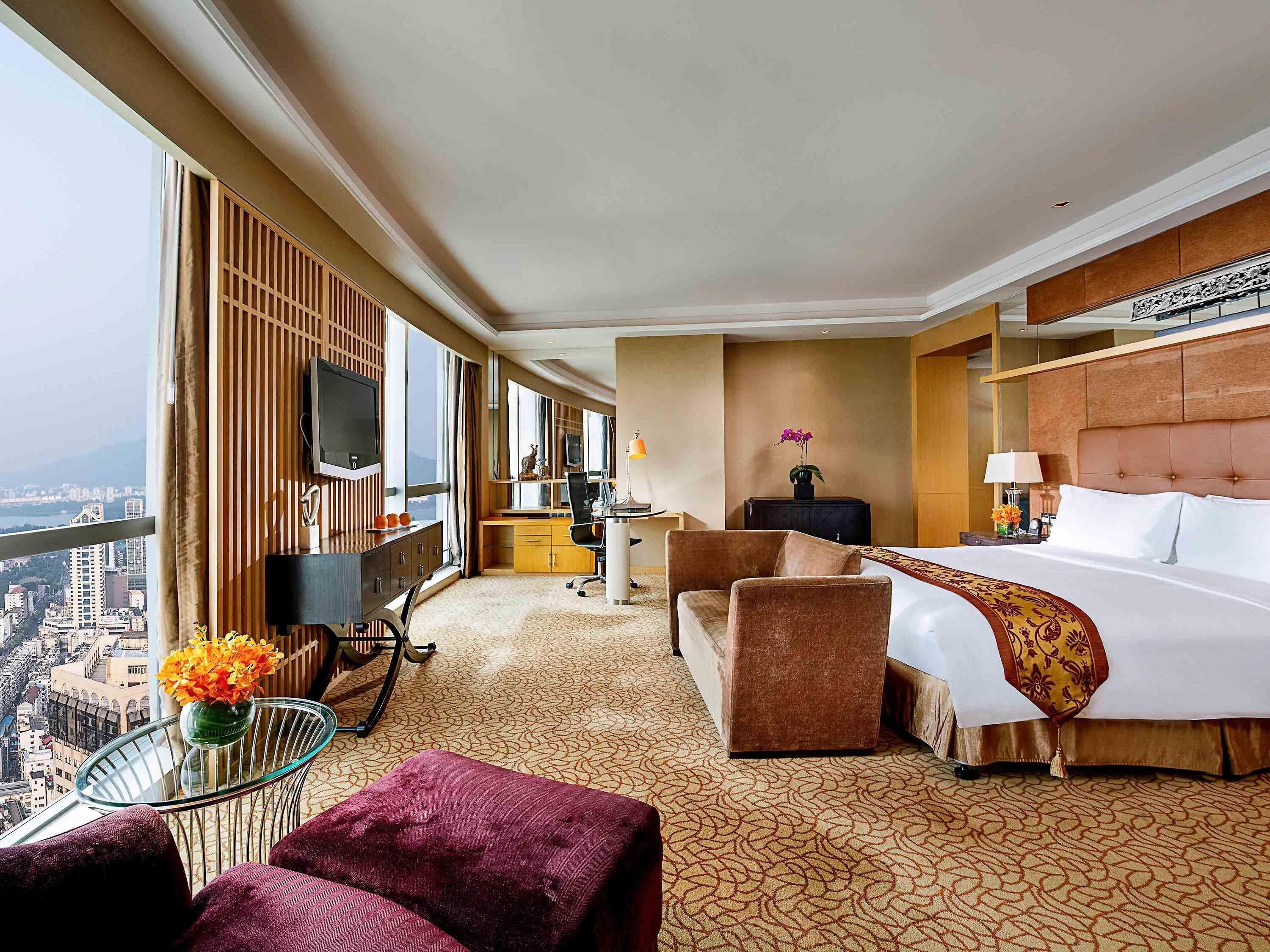 Ein Hotelzimmer mit einem großen Bett, einem Schreibtisch, einem Fernseher und Blick auf die Stadt.