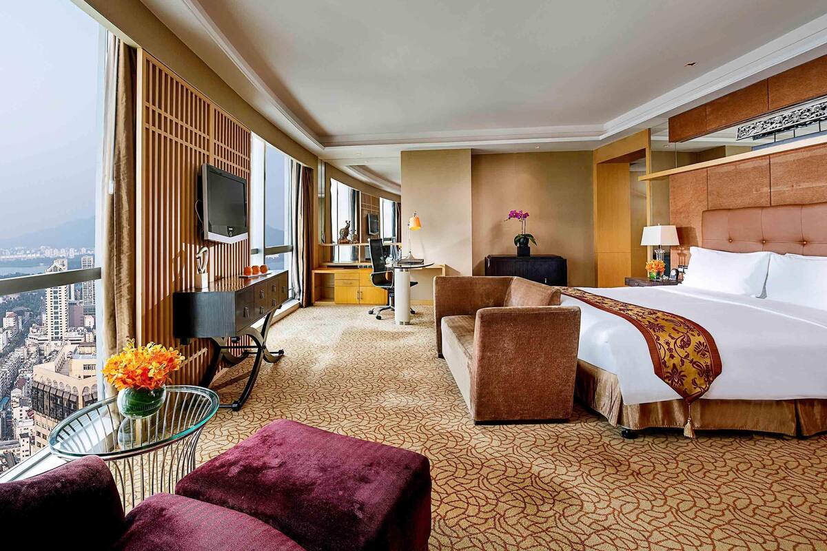 Habitación de hotel con una cama grande, un escritorio, un televisor y vistas a la ciudad.