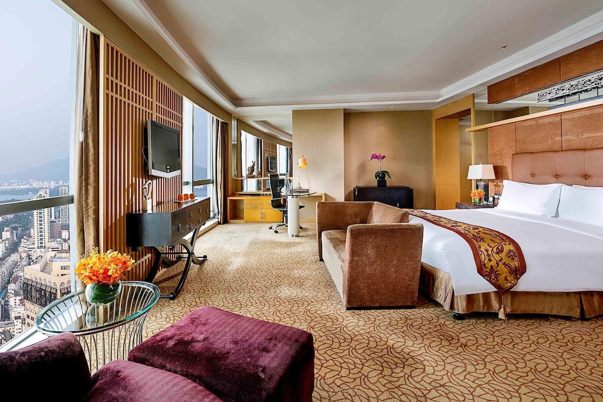 A hotel room with a large bed, a desk, a TV, and a view of the city.