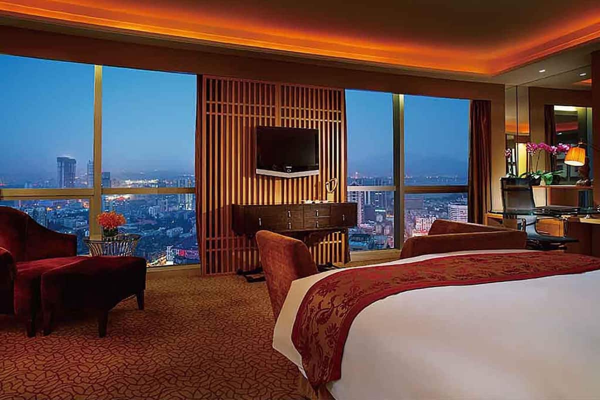 Habitación de hotel con una cama grande, televisión, escritorio y vistas a un paisaje urbano.
