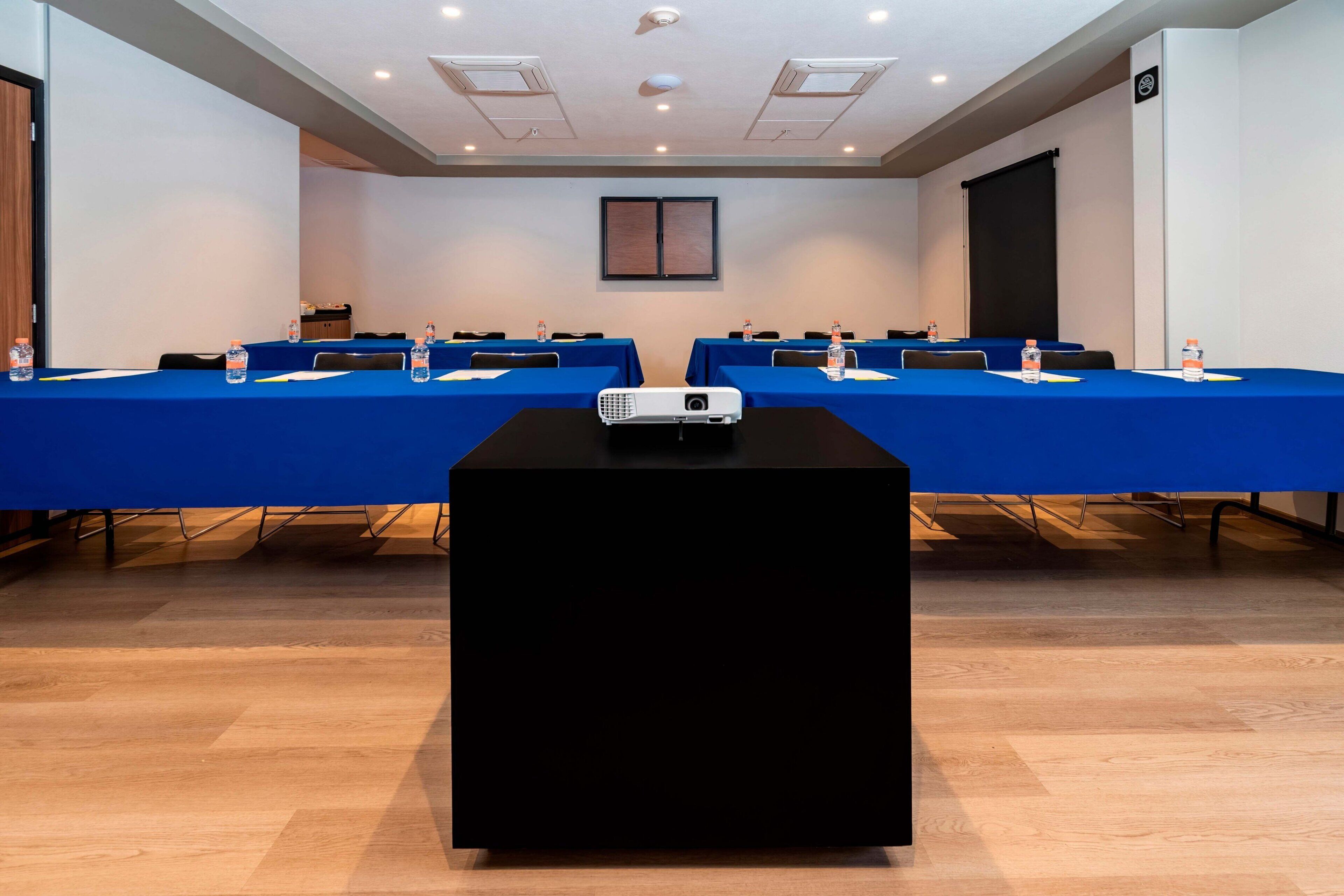 A conference room with a long table, blue tablecloths, water bottles, and a projector.