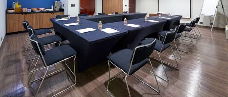 Un salón de conferencias con una larga mesa, sillas, una pizarra y una zona de kitchenette.