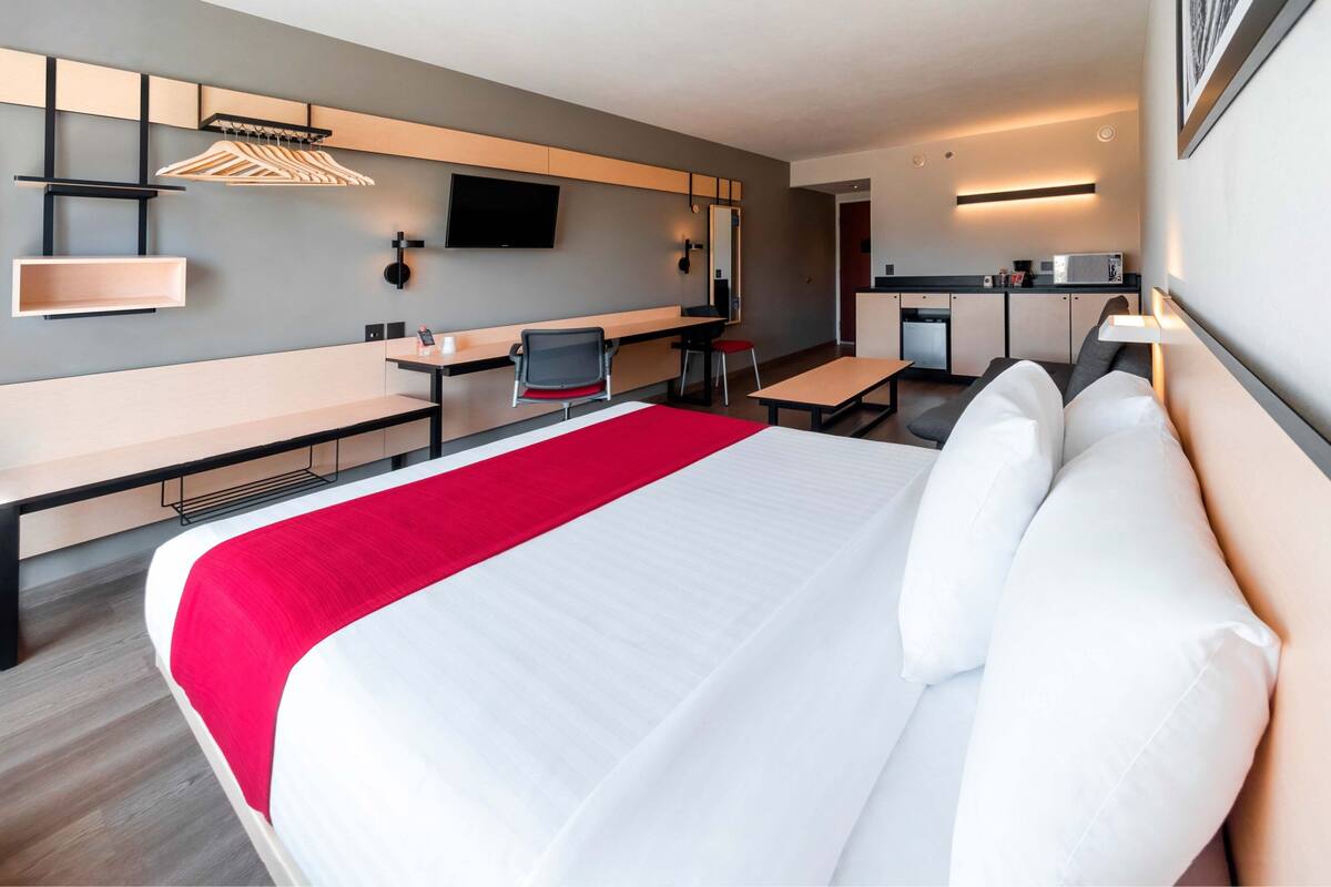Une chambre d’hôtel moderne équipée d’un grand lit, d’un bureau, d’une chaise et d’une kitchenette.