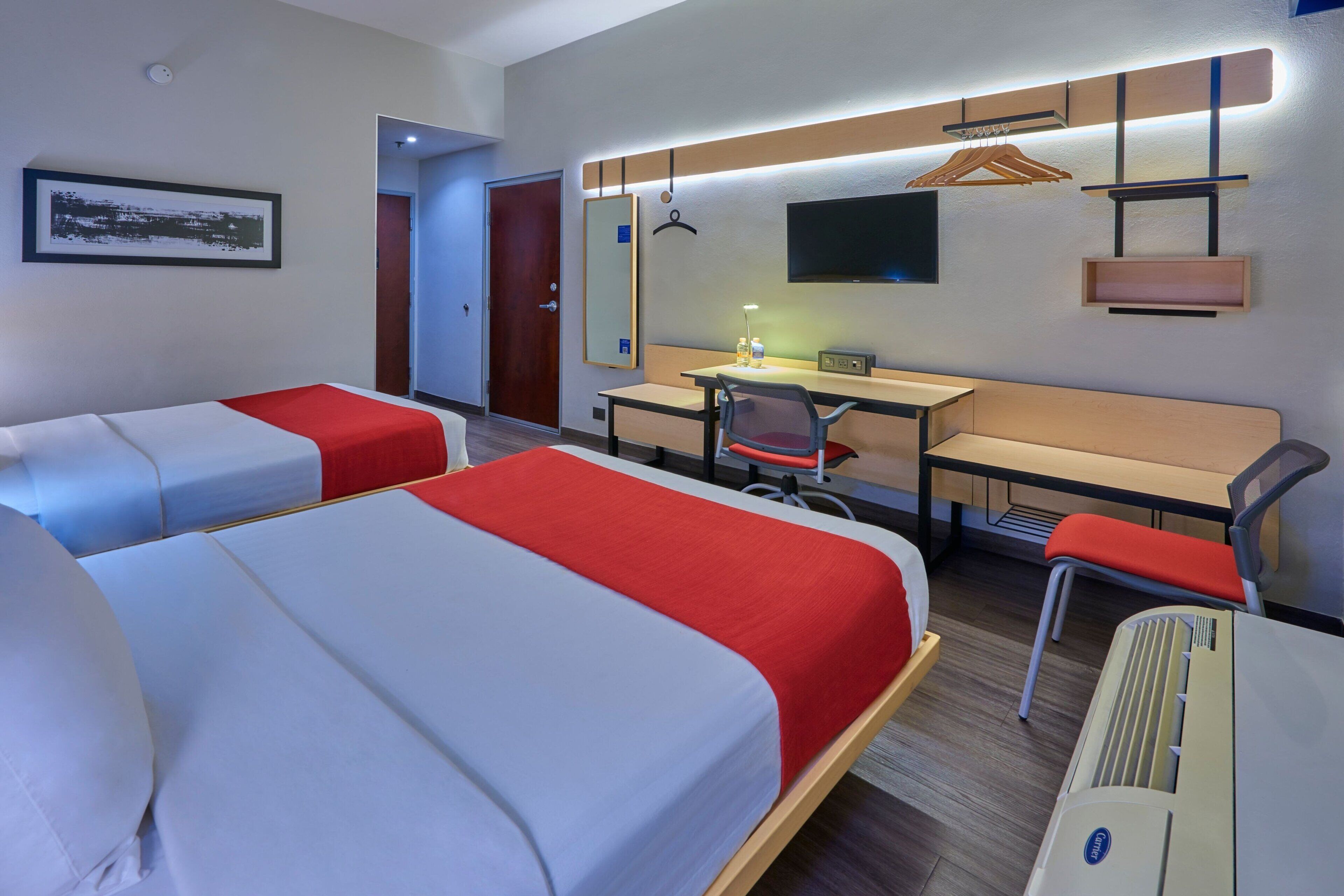 A hotel room with two beds, a desk, a chair, a TV, and a mirror.