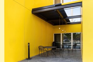 Un espace extérieur aménagé avec des sièges, un mur jaune, un toit en métal noir et une table avec des chaises.