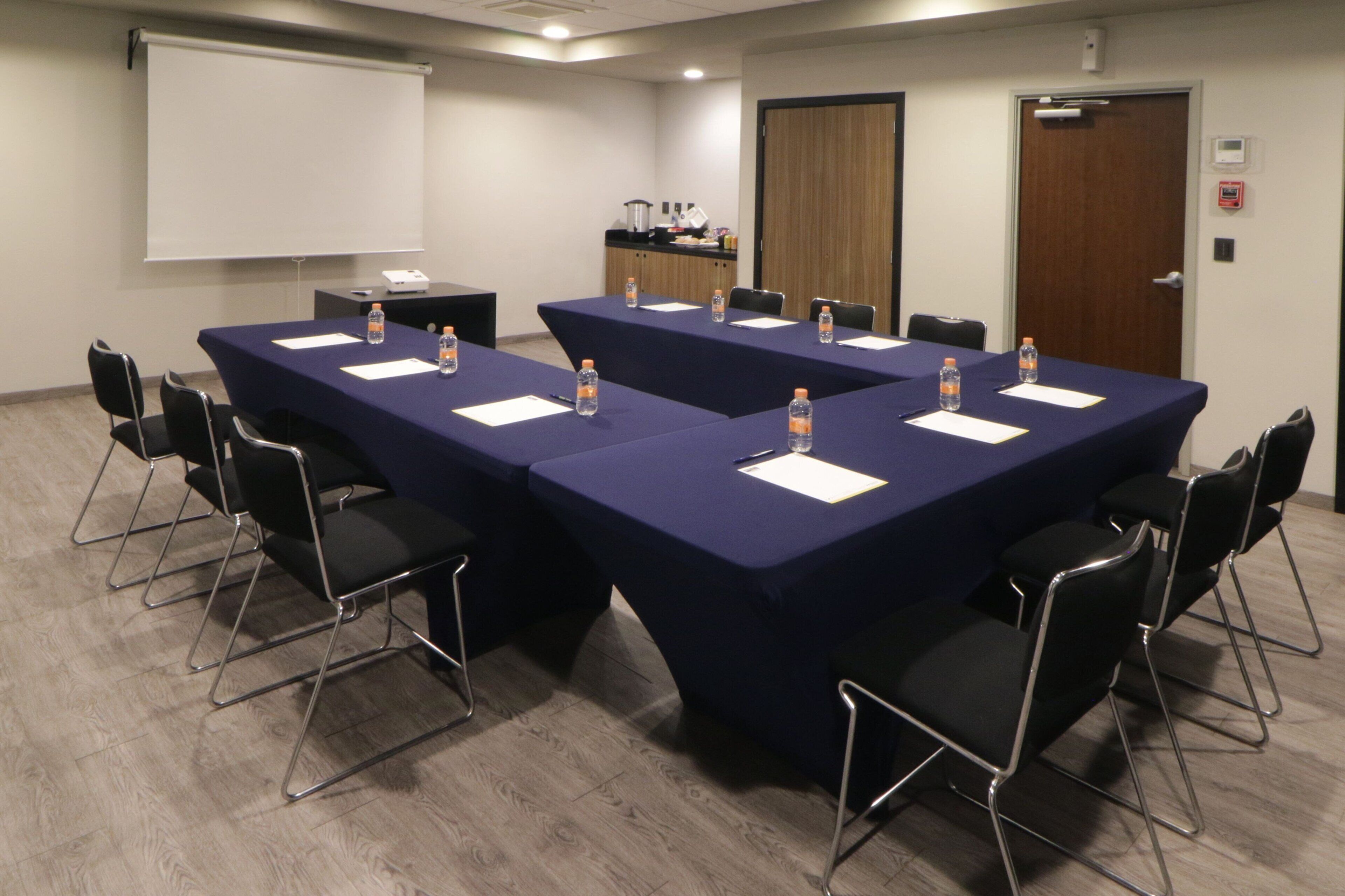 A conference room with a large table, chairs, a projector screen, and a water dispenser.