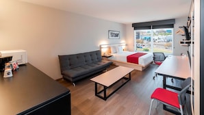 Une chambre d’hôtel moderne, dotée d’un canapé, d’un lit agrémenté d’une touche de rouge, d’une table à manger et offrant une vue sur la ville.