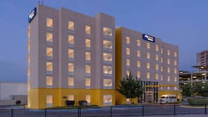Un hôtel moderne, doté de plusieurs étages, de grandes fenêtres et d’un espace de stationnement.