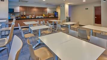 A modern dining area with multiple tables and chairs, a kitchen area with a coffee machine, and a refrigerator.