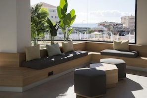 Un soggiorno moderno con un divano curvo, un poggiapiedi e un'ampia finestra vista mare e palazzi.