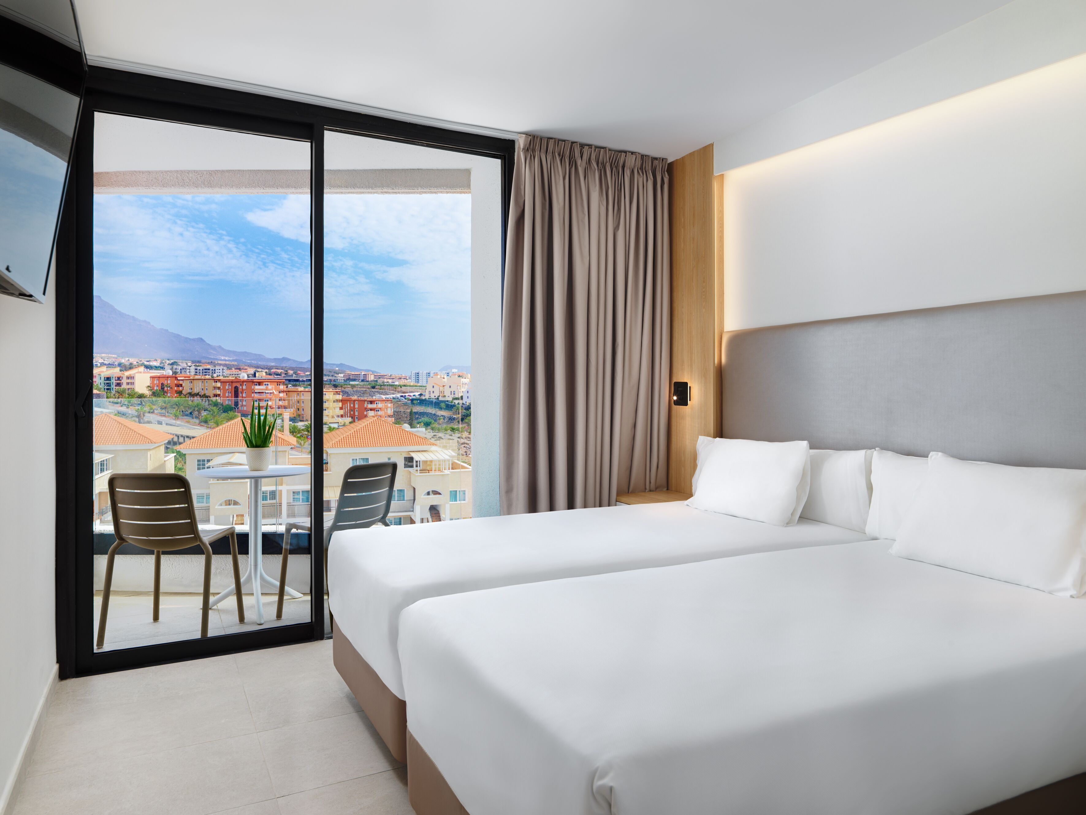 Een hotelkamer met balkon, een bed, een stoel en uitzicht op een stadsbeeld.