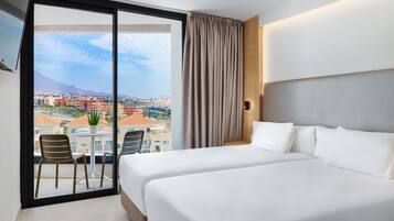 Een hotelkamer met balkon, een bed, een stoel en uitzicht op een stadsbeeld.
