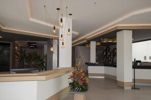 Un hall d’entrée moderne avec un comptoir d’accueil, des luminaires suspendus et une composition florale.