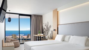 A hotel room with a large bed, a desk, a chair, a sofa, and a view of the sea. - Hotel Merlin Resort (Adeje)