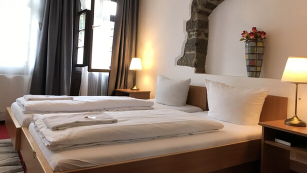 A hotel room with two beds, a stone arch wall, a vase with flowers, and a lamp on a nightstand. - Ritter Hotel (Frankfurt)