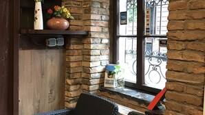 A cozy corner with wicker furniture, a stone wall, a window with a view, and a shelf with decorative items. - Ritter Hotel (Frankfurt)