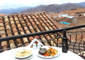 Una mesa con comida, una botella y vistas a tejados de tejas rojas y montañas.