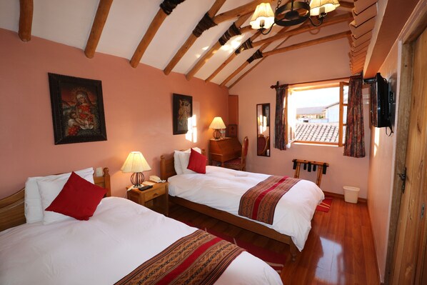 A hotel room with two beds, wooden beams on the ceiling, a window with curtains, and a television mounted on the wall. - Hotel & Mirador Los Apus (Cusco)