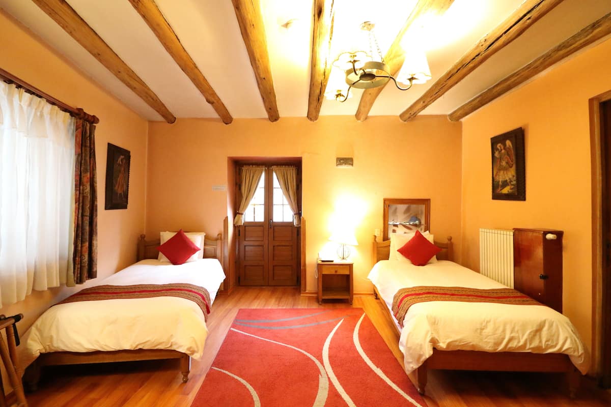 A room with two beds, wooden beams on the ceiling, a red carpet, and a door with curtains.