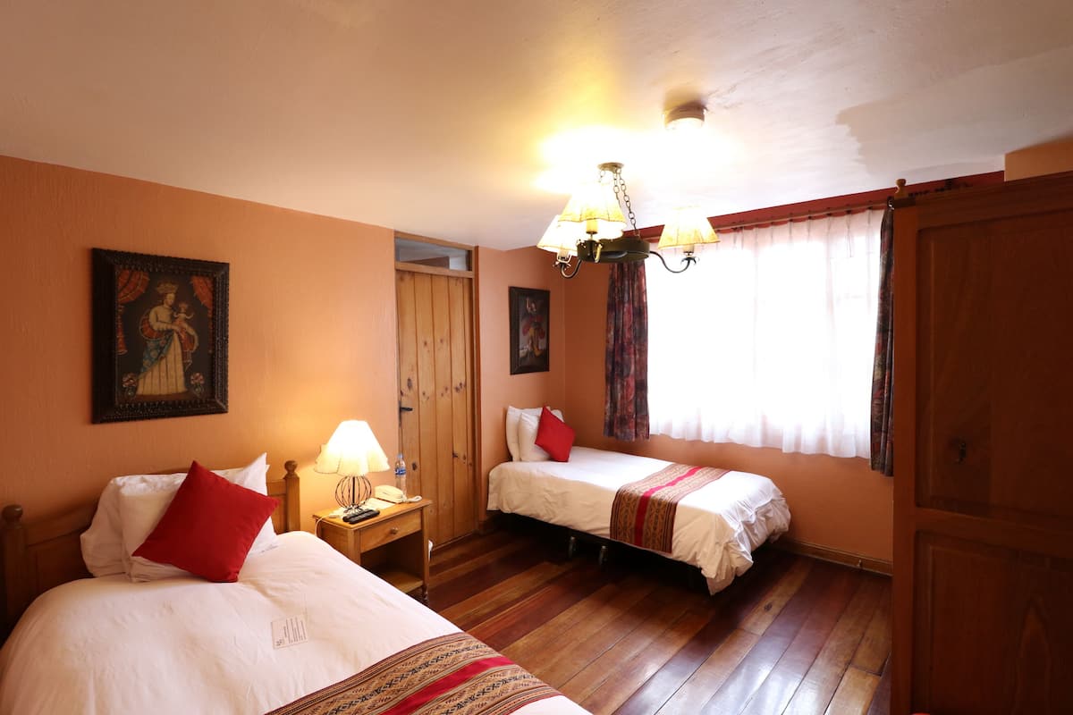 A room with two beds, wooden flooring, a chandelier, and a painting on the wall.