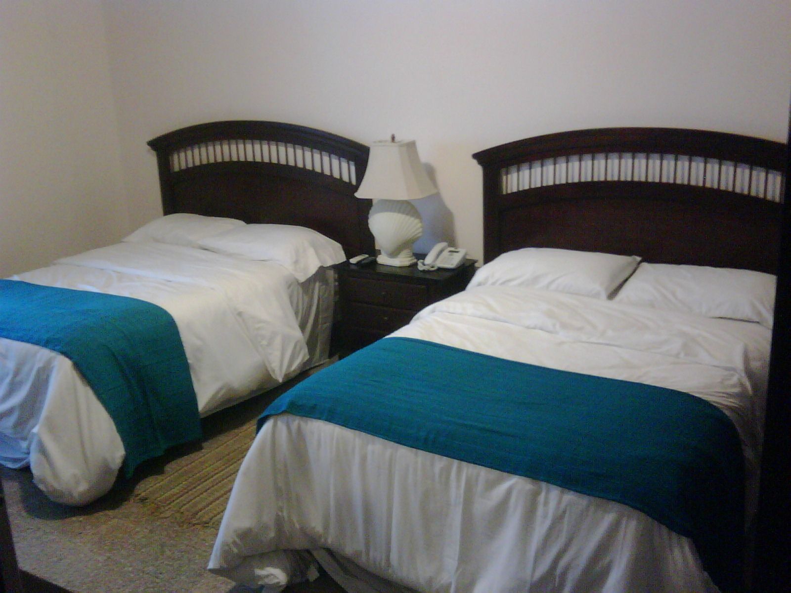 Dos camas individuales con cabeceros de madera, ropa de cama blanca y un detalle en azul.