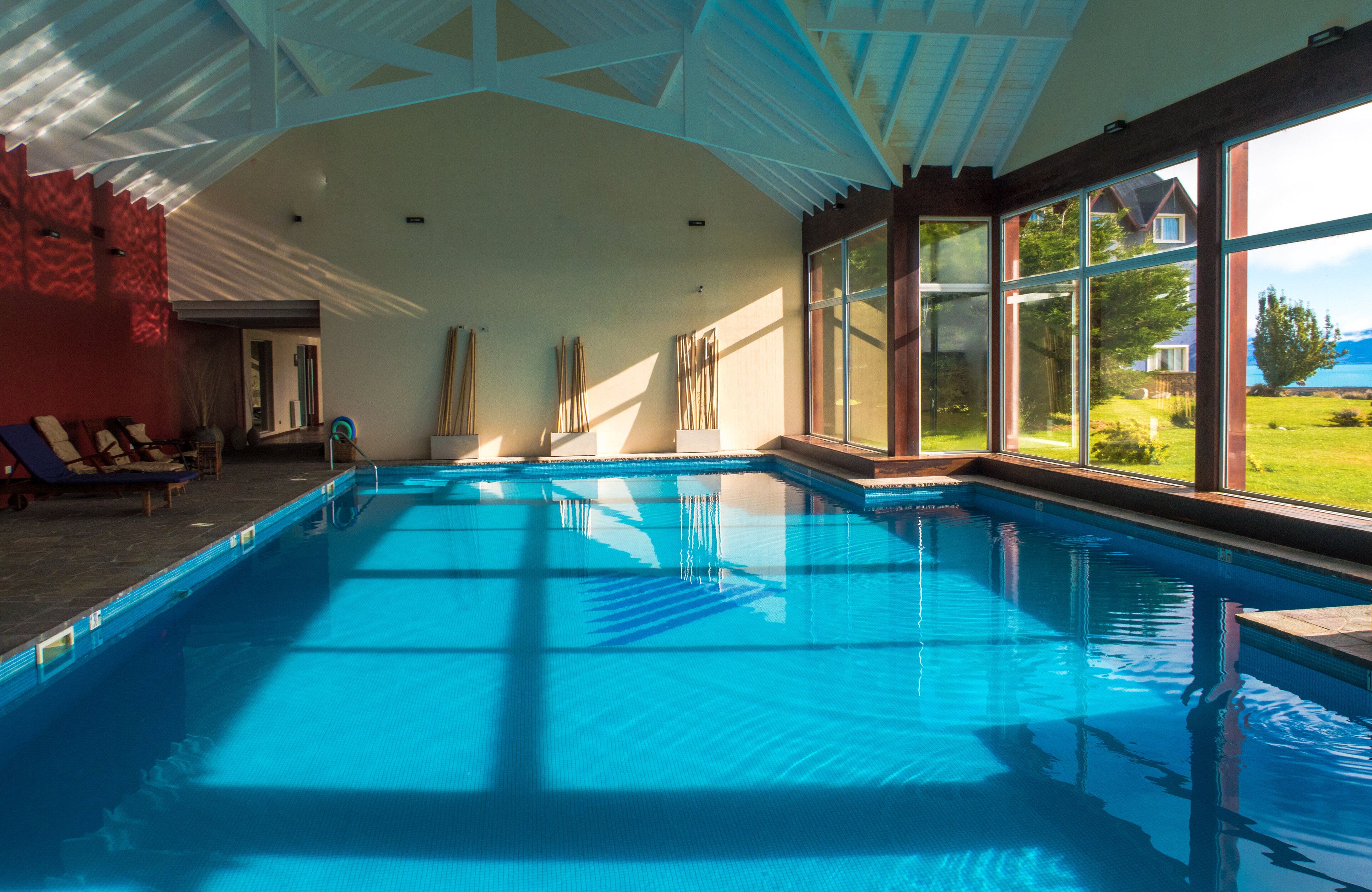 A large indoor swimming pool with clear blue water, surrounded by large windows offering views of the outdoors.